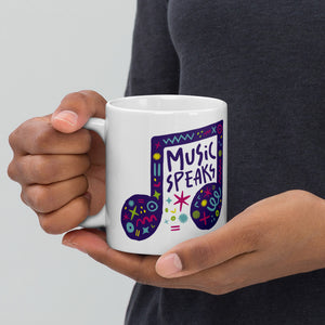 A person holding a white mug. The mug features a design with the words 'music speaks' in an illustrated musical note with sketchy elements around it.