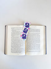 Load image into Gallery viewer, A bookmark placed inside a book. The bookmark features the words &quot;i love books&quot; with love shown shaped as a heart. The words are placed inside an illustrated book. 