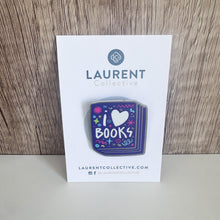 Load image into Gallery viewer, An enamel pin featured on a jean jacket. The pin has the words &#39;I love books&quot; with the word love shown as a heart. The words are featured inside an illustrated book, all in bright fun colors. The pin is shown on the Laurent Collective card backing it is mailed on. 