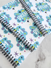 Load image into Gallery viewer, A closeup of three spiral notebooks are on a tabletop. The white spiral notebooks have black spiral binding. The pattern design features the word &quot;dream&quot; inside a cloud shape with sketchy elements around. 