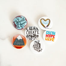 Load image into Gallery viewer, A set of six buttons on a white tabletop. The buttons feature word art illustrations with the words &quot;Live Your Story,&quot; &quot;Don&#39;t Give Up,&quot; &quot;Faith Hope Love,&quot; &quot;Create,&quot; &quot;Write,&quot; and &quot;World Changer.&quot;