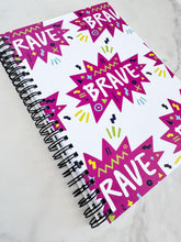 Load image into Gallery viewer, A spiral notebook on a tabletop. The white spiral notebook has black spiral binding. The pattern design features the word &quot;brave&quot; inside a hot pink star with sketchy elements around. 