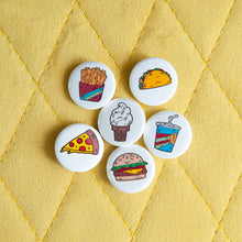 Load image into Gallery viewer, A set of six button pins on a yellow background. The pins feature illustrations of a taco, pizza slice, french fries, an ice cream cone, a milkshake and a burger. 