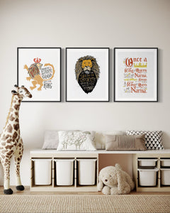 A set of three artwork prints hanging on a wall a playroom. The artwork is inspired by the Chronicles of Narnia. The first print reads "Course He Isn't Safe, But He's Good. He's the King." The second print reads "At The Sound of Your Roar, Sorrows Will Be No More," and the last print reads "Once a king or queen of Narnia, always a king or queen of Narnia."