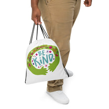 Load image into Gallery viewer, A person holding a white drawstring bag. The drawstring bag has the words &quot;Be Kind&quot; with green illustrated hands hugging the design with sketchy illustrations. 