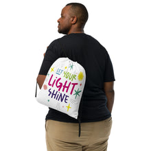 Load image into Gallery viewer, A man with a white drawstring bag on his back. The drawstring bag has the words &quot;Let Your Light Shine&quot; with sketchy illustrations around the words. 