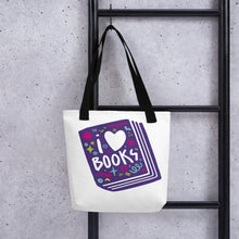 Load image into Gallery viewer, A white tote bag with black handles handing on a black ladder. The tote bag has a design with the words &#39;I love books&#39; with the word love shown as a heart. The words are inside an illustrated book. 