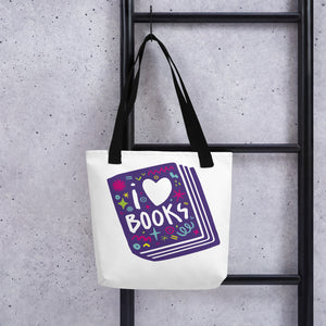 A white tote bag with black handles handing on a black ladder. The tote bag has a design with the words 'I love books' with the word love shown as a heart. The words are inside an illustrated book. 