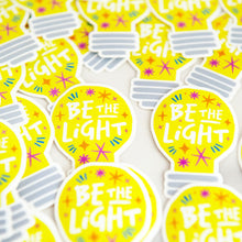 Load image into Gallery viewer, Die cut vinyl stickers with the words &quot;be the light&quot; inside an illustrated lightbulb.