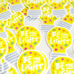 Die cut vinyl stickers with the words "be the light" inside an illustrated lightbulb.