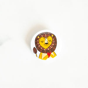 A button pin on a white tabletop. The button design features an illustrated lion. 