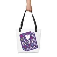 Load image into Gallery viewer, A person holding a white tote bag with black handles. The tote bag has a design with the words &#39;I love books&#39; with the word love shown as a heart. The words are inside an illustrated book. 