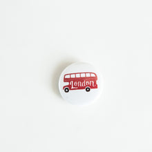 Load image into Gallery viewer, A button on white tabletop. The button features an illustration of a double decker bus. 