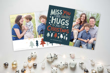Load image into Gallery viewer, A photo of a Christmas card showing the front and back of the card laying on a white surface. To the bottom of the cards are silver and white small ornaments. The front of the card features a photo on the right side and on the left side are the words “ Miss you and sending hugs to you this Christmas” with illustrated trees below the words. The back of the card features two photos with illustrated trees at the bottom.