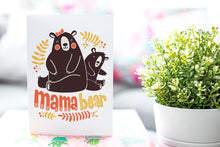 Load image into Gallery viewer, A greeting card is on a table top with a gift in pink wrapping paper. Next to the gift is a white plant pot with a green plant. The card features the words “Mama Bear” with an illustrated mama bear and baby bear.