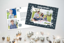 Load image into Gallery viewer, A photo of a Christmas card showing the front and back of the card laying on a white surface. To the bottom of the cards are silver and white small ornaments. The front of the card features a photo with a frame around it with illustrated snowflakes. Above the photo reads “Merry Christmas” and below the photo you can add your family name. The back of the card features two photos, illustrated snowflakes and a place to add a family update. 