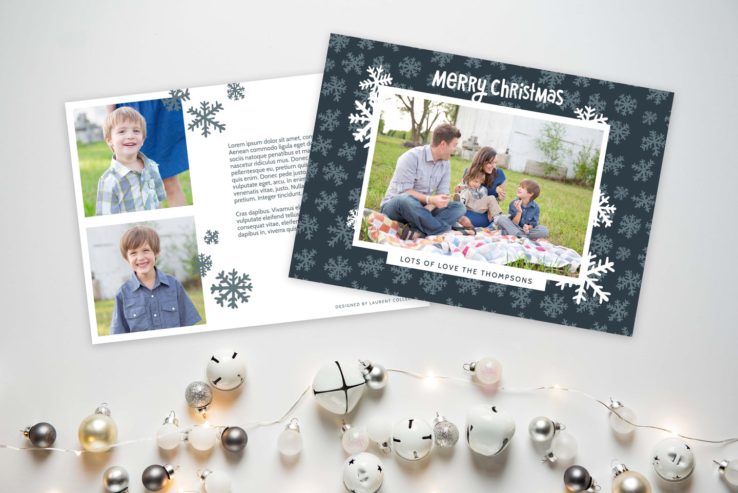 A photo of a Christmas card showing the front and back of the card laying on a white surface. To the bottom of the cards are silver and white small ornaments. The front of the card features a photo with a frame around it with illustrated snowflakes. Above the photo reads “Merry Christmas” and below the photo you can add your family name. The back of the card features two photos, illustrated snowflakes and a place to add a family update. 