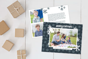 A photo of a Christmas card showing the front and back of the card laying on a white surface. Brown wrapped small gifts are to the left of the cards. The front of the card features a photo with a frame around it with illustrated snowflakes. Above the photo reads “Merry Christmas” and below the photo you can add your family name. The back of the card features two photos, illustrated snowflakes and a place to add a family update.
