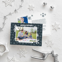 Load image into Gallery viewer, A photo of a double-sided Christmas card showing the front and back of the card laying on a white surface. Around the two sides of the card are surrounded with Christmas items. The front of the card features a photo with a frame around it with illustrated snowflakes. Above the photo reads “Merry Christmas” and below the photo you can add your family name. The back of the card features two photos, illustrated snowflakes and a place to add a family update. 