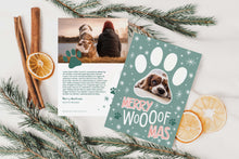 Load image into Gallery viewer, A photo of a double-sided Christmas card showing the front and back of the card laying on a white surface. Around the two sides of the card are pine needles, cinnamon sticks and dried oranges. The front of the card features a photo inside a paw shaped frame. Around the photo are white stars and below are the words “Merry Woofmas.” The back of the card features one photo with a dog paw illustration and space to add an update. 