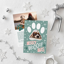 Load image into Gallery viewer, A photo of a double-sided Christmas card showing the front and back of the card laying on a white surface. Around the two sides of the card are surrounded with Christmas items. The front of the card features a photo inside a paw shaped frame. Around the photo are white stars and below are the words “Merry Woofmas.” The back of the card features one photo with a dog paw illustration and space to add an update.