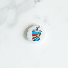 Load image into Gallery viewer, A button pin on a white tabletop. The pin features an illustration of a milkshake cup.