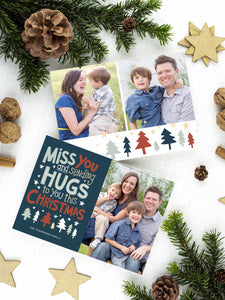 A photo of a two-sided Christmas card showing the front of the card on top of a brown wrapped gift on a white tabletop. Around the gift are pine needles, pinecones and wood star ornaments. The front of the card features a photo on the right side and on the left side are the words “ Miss you and sending hugs to you this Christmas” with illustrated trees below the words. The back of the card features two photos with illustrated trees at the bottom.