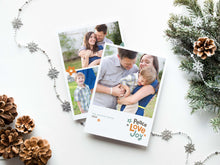 Load image into Gallery viewer, A photo of a double-sided Christmas card showing the front and back of the card laying on a white surface. Around the two sides of the card are pine cones, pine needles and a string of silver snowflake garland. The front of the card features a photo with the words “Peace Love joy” to the bottom right and space to the bottom left to put your family names. The words feature some modern illustrated flowers around it. The back of the card features three photos with modern illustrated flowers.