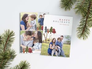 A photo of a Christmas card showing the front and back of the card laying on a white surface. Around the two sides of the card are pine needles. The front of the card features a photo on the bottom and on the top it reads “Happy Holidays, The Franklins” with illustrated modern pine trees. The back of the card features three photos.