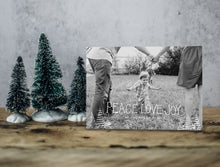 Load image into Gallery viewer, A photo of a one-sided Christmas card showing the front of the card standing up with three small Christmas trees next to it. The card features a photo with the words “Peace Love Joy” over the photo and a space to put your family name below. There are illustrated modern trees on the bottom. 