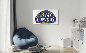 A large flag featured on a wall of a kids playroom. The white flag features the words "stay curious" featured inside a a purple shape with sketchy illustrations around. 