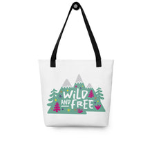 Load image into Gallery viewer, A white tote bag with black handles on a white background. The tote bag has the design with the words &#39;wild and free&#39; with the words inside illustrated mountains with illustrated trees around the words. 