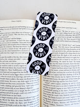 Load image into Gallery viewer, A bookmarks placed inside a book. The bookmark features the words &quot;good vibes&quot; inside an illustrated vinyl record.