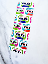 Load image into Gallery viewer, A bookmark placed on a tabletop. The bookmark features the words &quot;good vibes&quot; inside an illustrated cassette tape. 