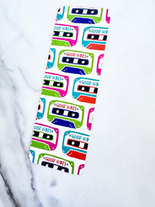 A bookmark placed on a tabletop. The bookmark features the words "good vibes" inside an illustrated cassette tape. 