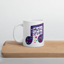 Load image into Gallery viewer, A white mug on a wood board. The mug features a design with the words &#39;music speaks&#39; in an illustrated musical note with sketchy elements around it.