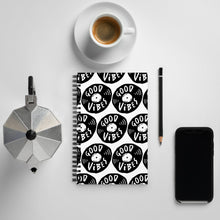 Load image into Gallery viewer, A spiral notebook on a tabletop with a coffee mug and phone around it. The white spiral notebook has black spiral binding. The pattern design features the words &quot;good vibes&quot; inside an illustrated vinyl record.  