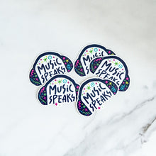 Load image into Gallery viewer, Vinyl die cut stickers with the words &quot;music speaks&quot; with illustrated headphones around the words. 