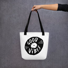 Load image into Gallery viewer, A person holding a white tote bag with black handles. The bag features a design with the words &#39;good vibes&#39; inside an illustrated vinyl record. 