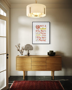 Artwork in a black frame with the with a white matte. The frame is on a wall in an entryway. The artwork features hand drawn lettering of the Narnia quote "Once a king or queen of Narnia, always a king or queen of Narnia."