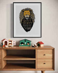 Artwork in a black frame with the with a white matte. The frame is on a wall above a dresser with children's items on top. The artwork features an illustrated Aslan (the lion from Chronicles of Narnia). Inside the lion the Narnia quote is featured reading “At The Sound of Your Roar, Sorrows Will Be No More.”