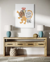 Load image into Gallery viewer, A white canvas with artwork hanging on a wall above an entryway table with lamps on it. The artwork features an illustrated lion with a crown and reads &quot;Course He Isn&#39;t Safe, But He&#39;s Good. He&#39;s the King.&quot;