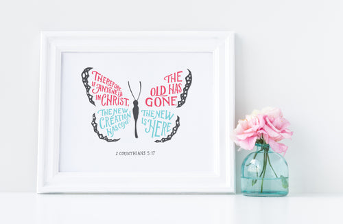 Artwork in a white frame with the with a white matte. The frame is leaning on a white counter with a pink flower in a blue case next to it. The hand drawn artwork features the scripture verse 