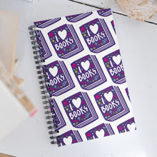 Load image into Gallery viewer, A spiral notebook on a white, wood tabletop. The white spiral notebook has black spiral binding. The pattern design features the words &quot;I love books&quot; inside an illustrated book with the word love as a heart. 