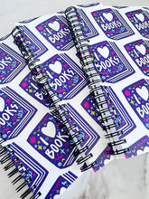 Load image into Gallery viewer, A closeup of three spiral notebooks are on a tabletop. The white spiral notebooks have black spiral binding. The pattern design features the words &quot;I love books&quot; inside an illustrated book with the word love as a heart. 