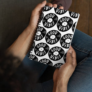 A spiral notebook being held by a person. The white spiral notebook has black spiral binding. The pattern design features the words "good vibes" inside an illustrated vinyl record.  