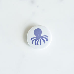 A button on a white tabletop. The button features an illustration of an octopus. 