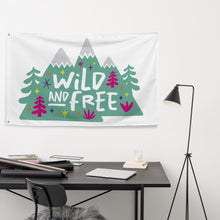 Load image into Gallery viewer, A large white flag featured on a wall above a desk. The white flag features the words &#39;wild and free&#39; inside illustrated mountains with sketch trees and other elements around.