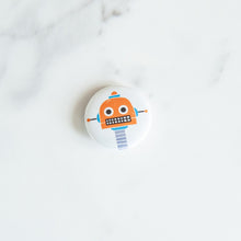 Load image into Gallery viewer, A button pin on a white tabletop. The button features an illustration of a orange robot.