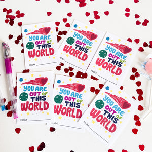 Six classroom valentines on a white tabletop. The valentine reads "You are out of this world" with space-themed illustrations. 